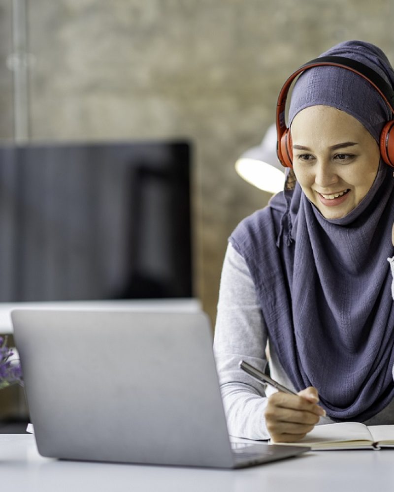 Muslim businesswoman wearing a hijab looks at camera working Online Tutoring. Young Muslim woman teacher having a video call with students